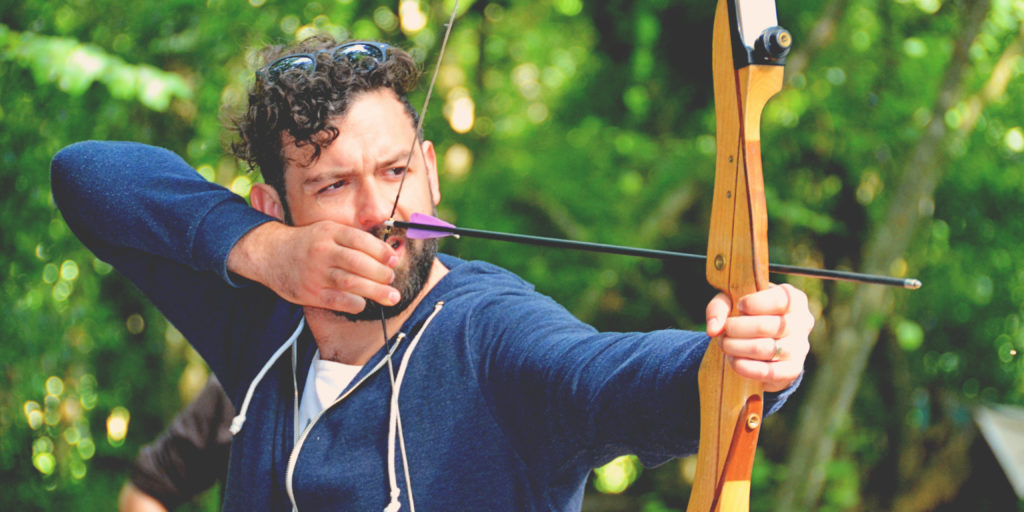 a man drawing back the string on a bow in the woods