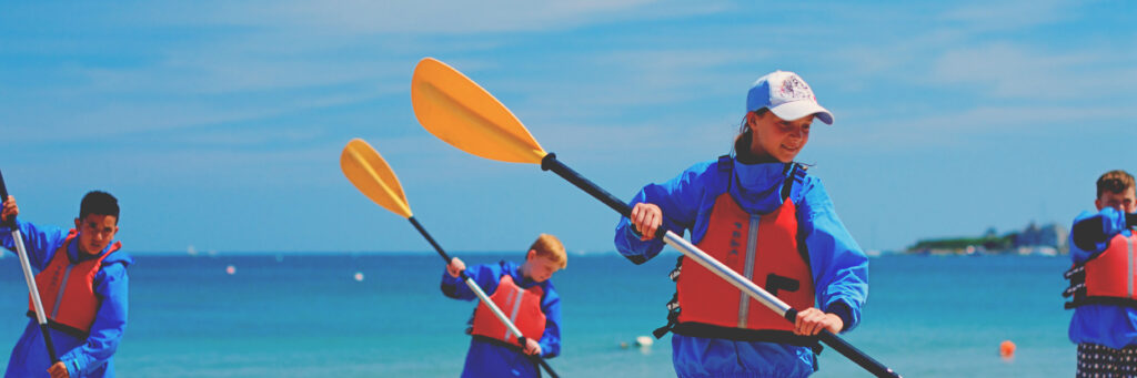 Four kids learning how to paddle on beach Kids Club on a very sunny day with blue skies